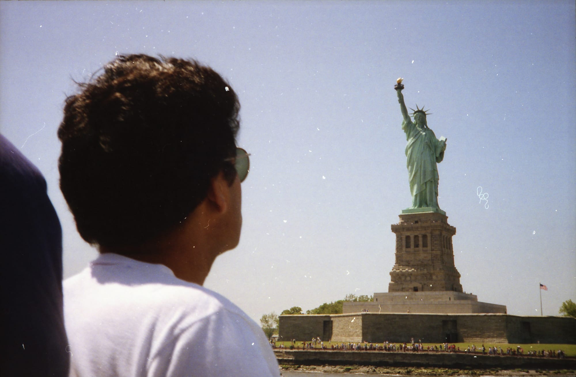 Young man in sunglasses, from behind. The Statue of Liberty, New York