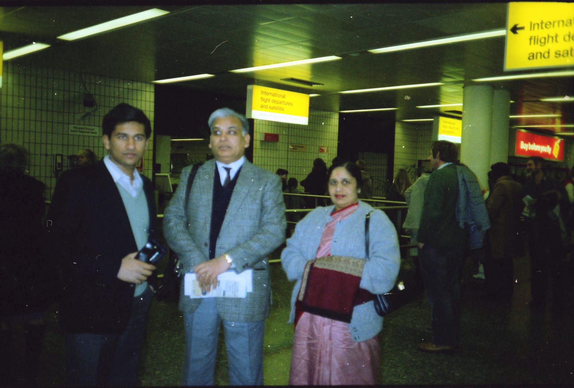 Three at departures, one holding a camera. Heathrow Airport