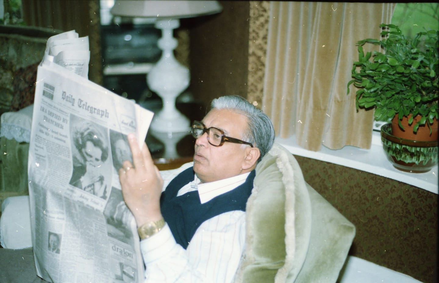 Papaji in his armchair, holding the Daily Telegraph open, in a navy slipover over a pinstriped shirt.