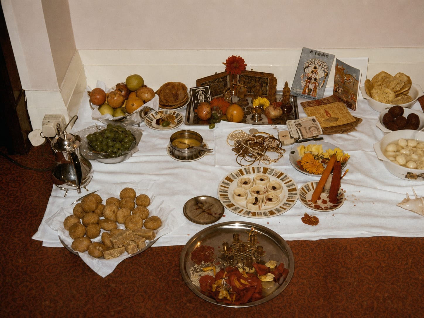 Diwali puja laid out on a white sheet with sweets, fruit and a silver thali in an English home